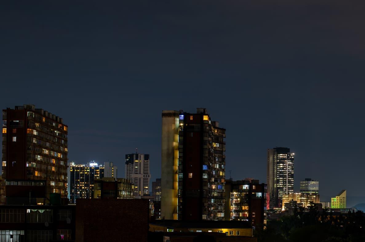 City Lights: The Sunnyside Horizon A wide urban landscape showcasing illuminated high-rise apartment blocks glowing soft yellow and blue against the night sky.