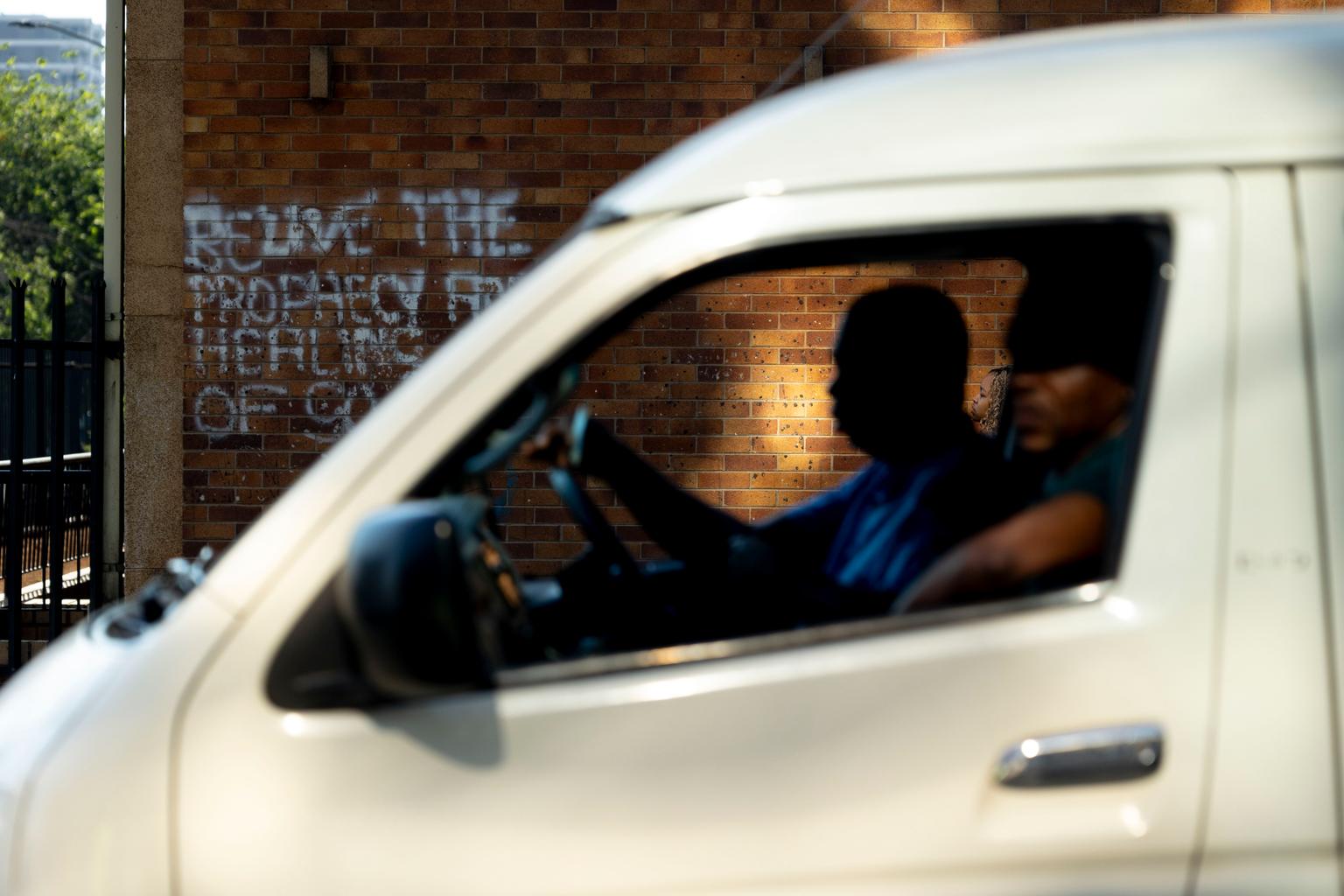 A taxi with a passenger drives past grafiti in the morning light
