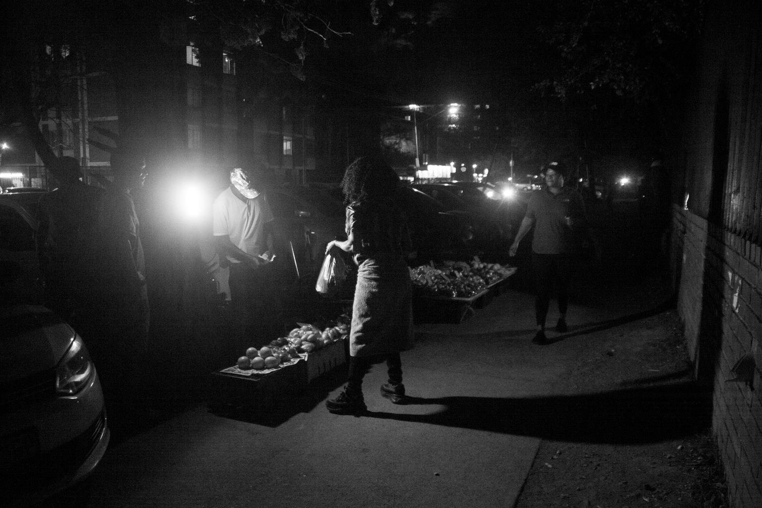 Shades of Gray in Sunnyside:   The high-contrast lighting of the street lamp and the deep shadows emphasize the form of the vendor and the customer.