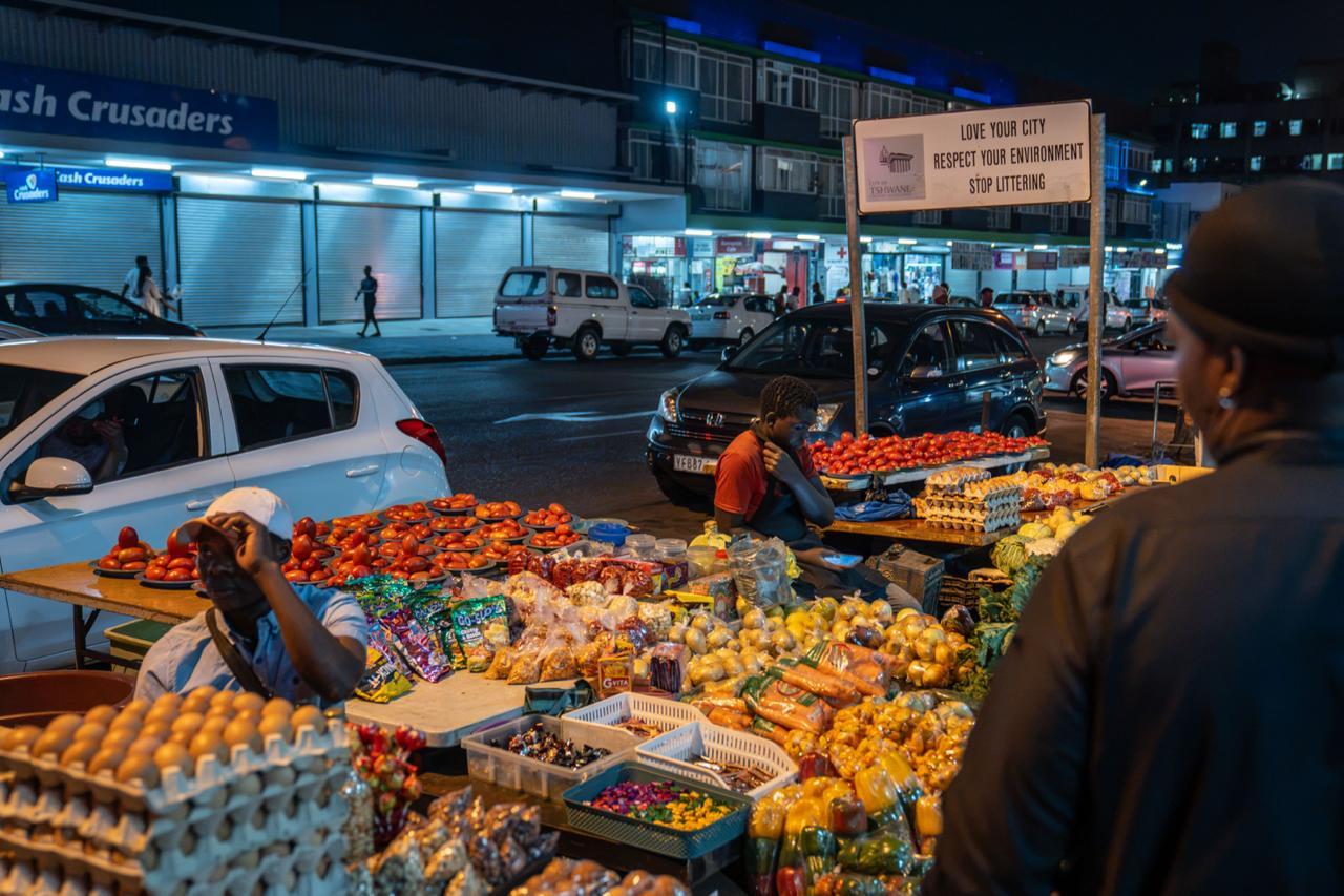 Markets and Public Messages:  A vendor sits amidst a colorful display of fresh tomatoes and other vegetables. 