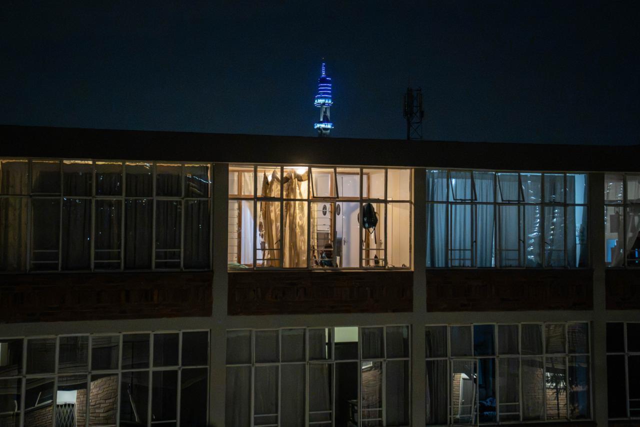 Illuminated Living: Apartments & City Skyline Warm interior light fills an apartment balcony overlooking the night sky and the iconic Telkom tower