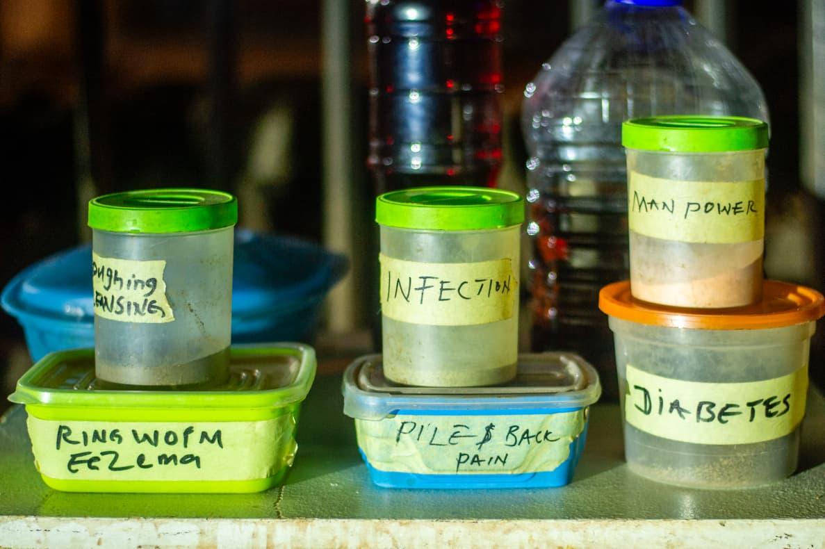 Traditional Remedies: Street Pharmacy Clear plastic containers labeled with handwritten notes display traditional herbal mixtures lined up neatly on a market shelf.