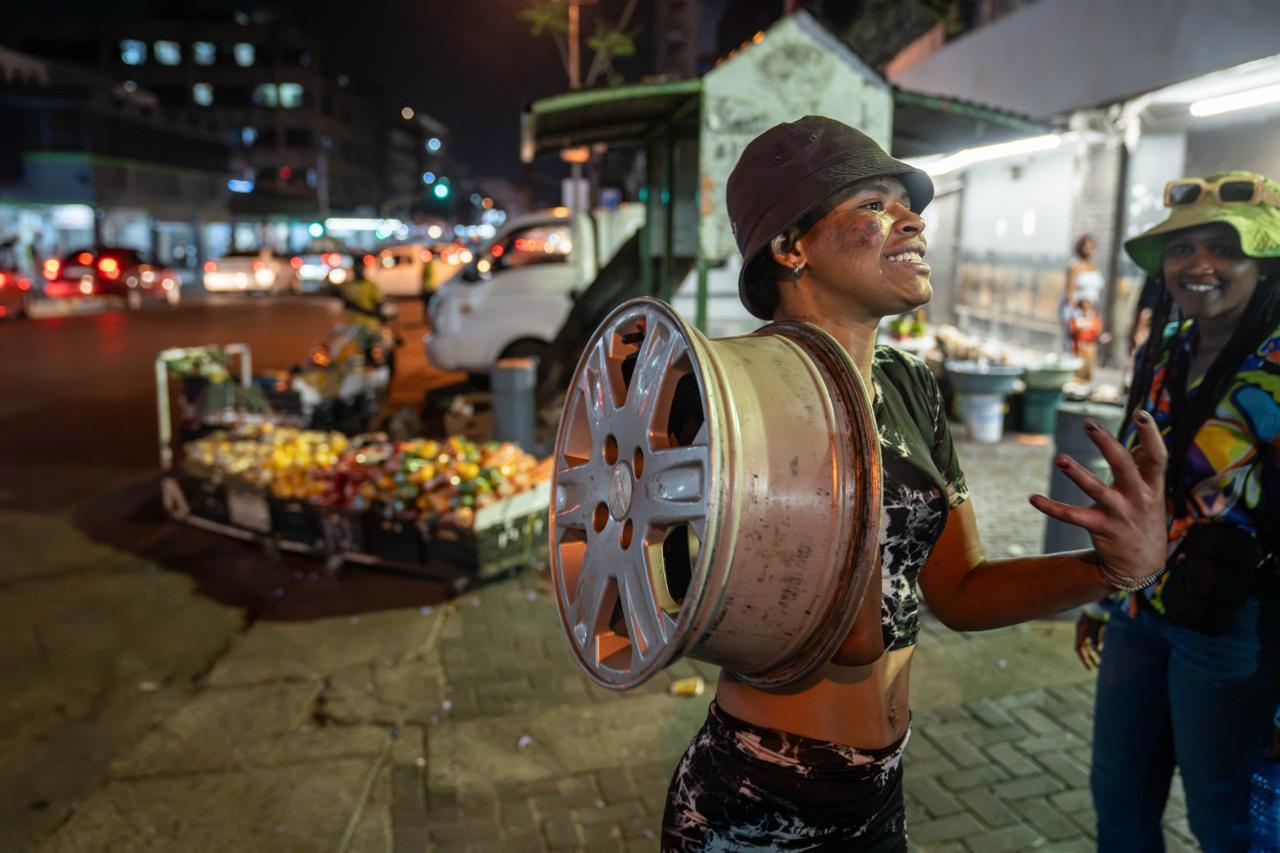 Woman in the Spotlight:  A woman walking with the rim of a car wheel. 