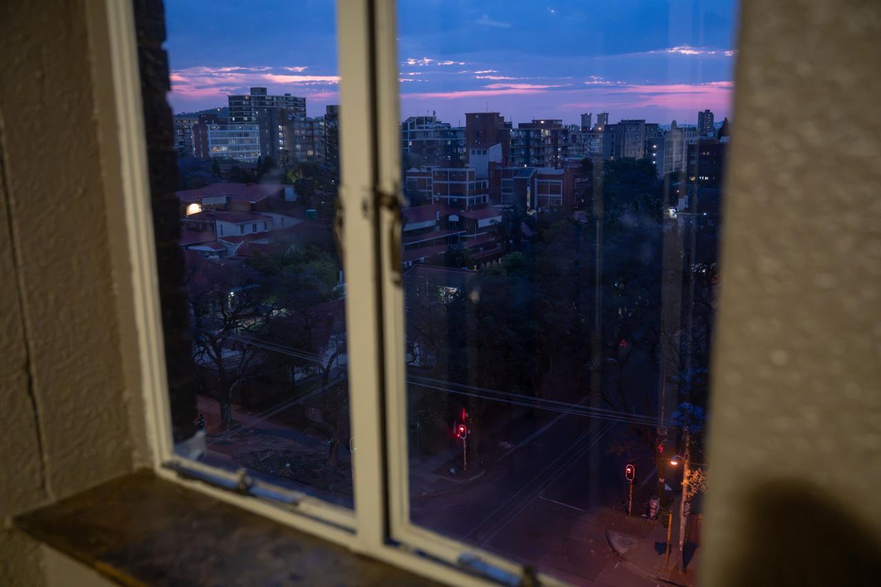 Dusk Frame: View from Within Framed through a high-rise window, the setting sun paints the evening sky in deep purples and pinks over the sprawling street below.
