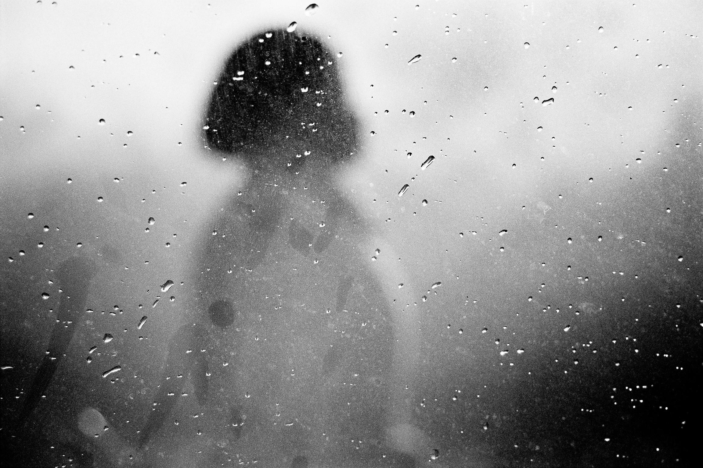 Person's blurred silhouette seen through steamed glass covered in water droplets, Cape Town.