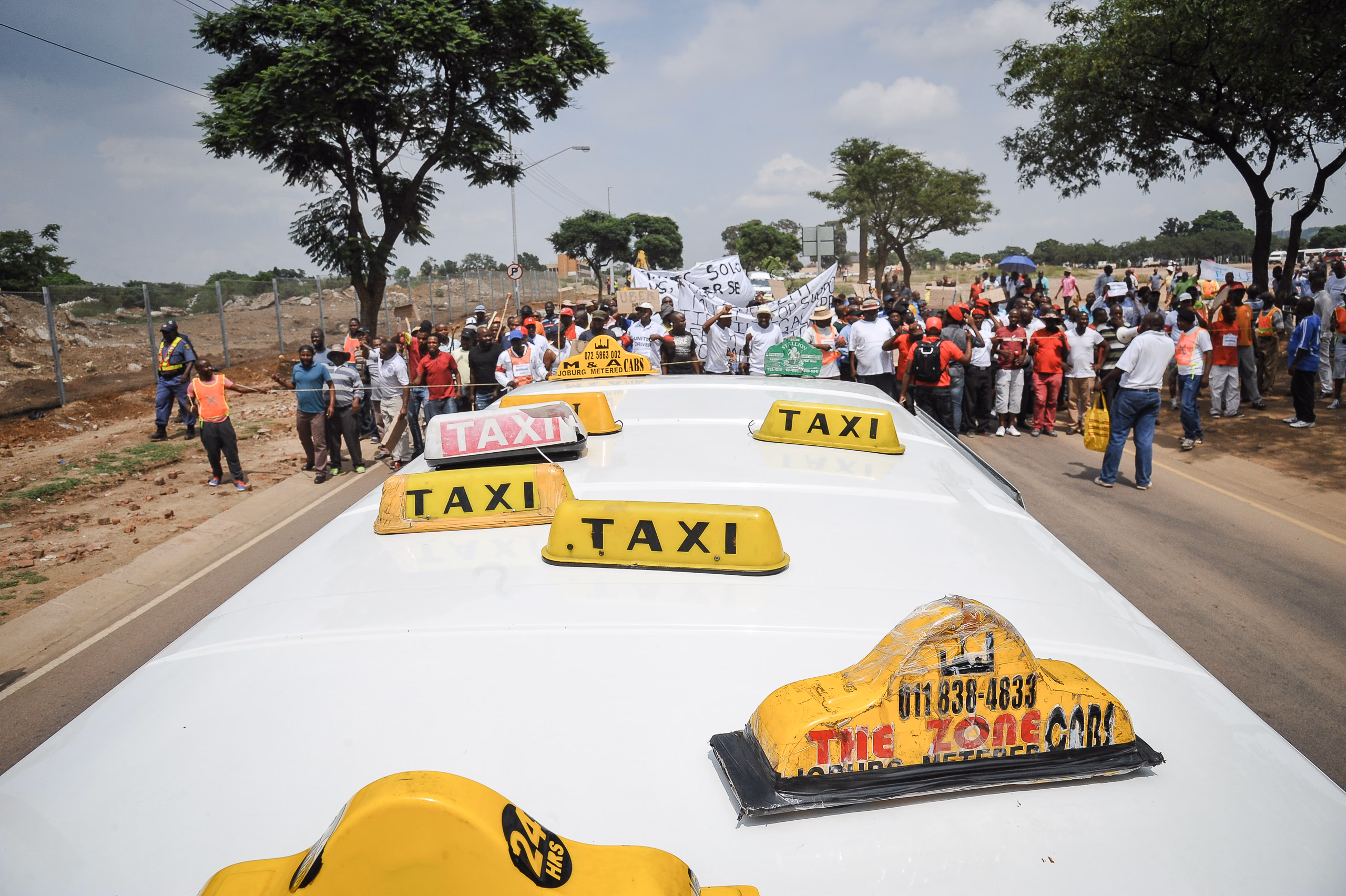 Elevated view over the roofs of yellow minibus taxis, a crowd marching along the road behind them.