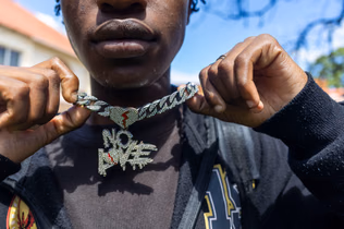 Close-up of a young man holding out a diamante chain with a broken-heart clasp and a pendant reading "NO LOVE".