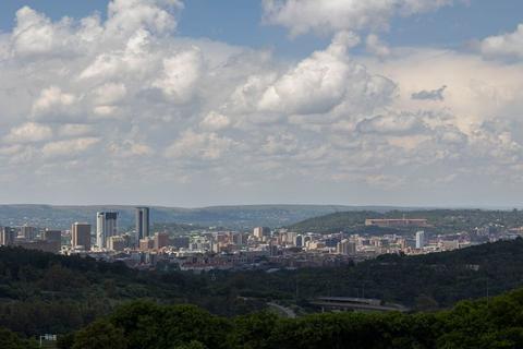 Wide view of the Pretoria city centre skyline from a wooded ridge, with the Union Buildings on the hillside to the right and cumulus cloud above.