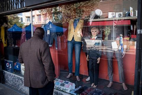 Clothing and mannequins displayed on the pavement outside a shop as a man walks past.