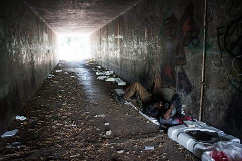 A dark underpass strewn with rubbish, daylight at the far opening.