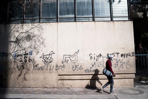 A man wlaks past a wall covered in graffiti lettering, blank windows above.