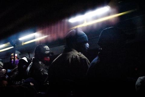 Silhouetted figures in a dark interior of transport cut by a hard streak of light.