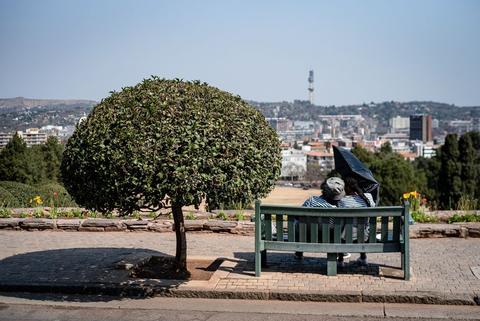 A person sits on a bench beneath a tree on a hillside, the city spread out below.