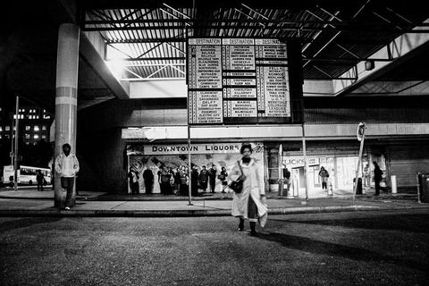 Central Cape Town bus terminus and a large bus destination board listing dozens of place names, with people waiting beneath it outside shuttered shops.