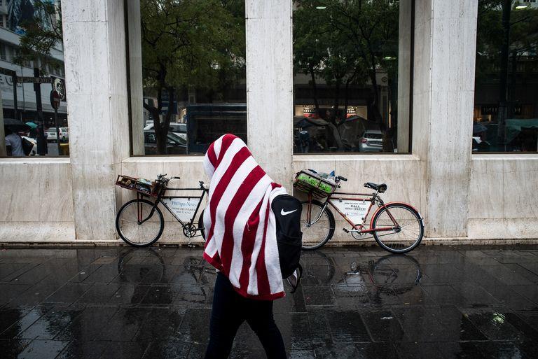 A person wrapped in a red and white striped blanket walks through a concrete colonnade past a parked bicycle.
