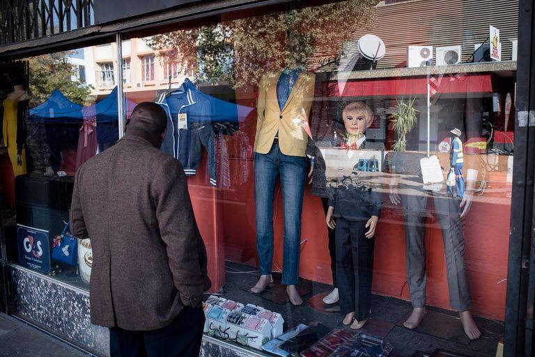 Clothing and mannequins displayed on the pavement outside a shop as a man walks past.