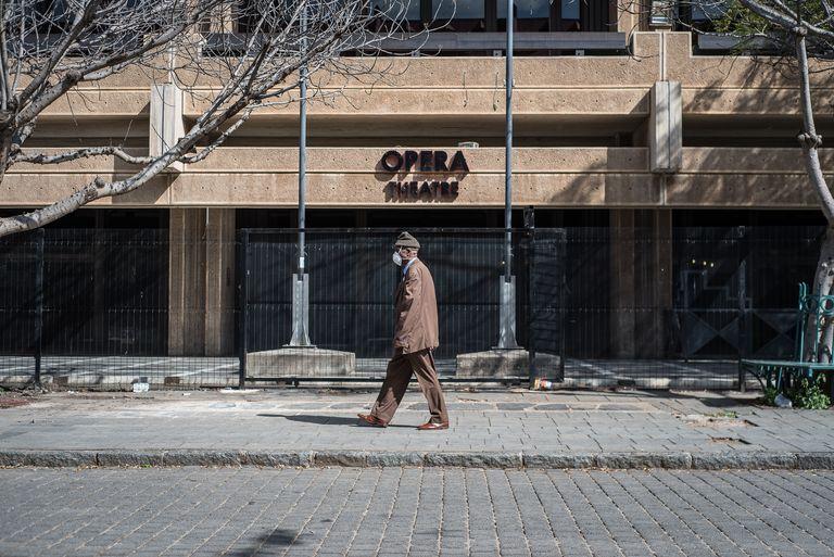 A man walks along an empty pavement past a building signed Opera, one pigeon in the air.