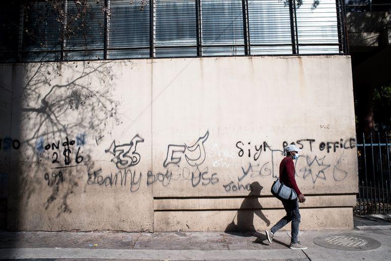 A man wlaks past a wall covered in graffiti lettering, blank windows above.