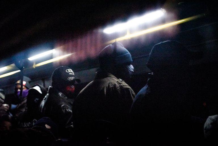 Silhouetted figures in a dark interior of transport cut by a hard streak of light.